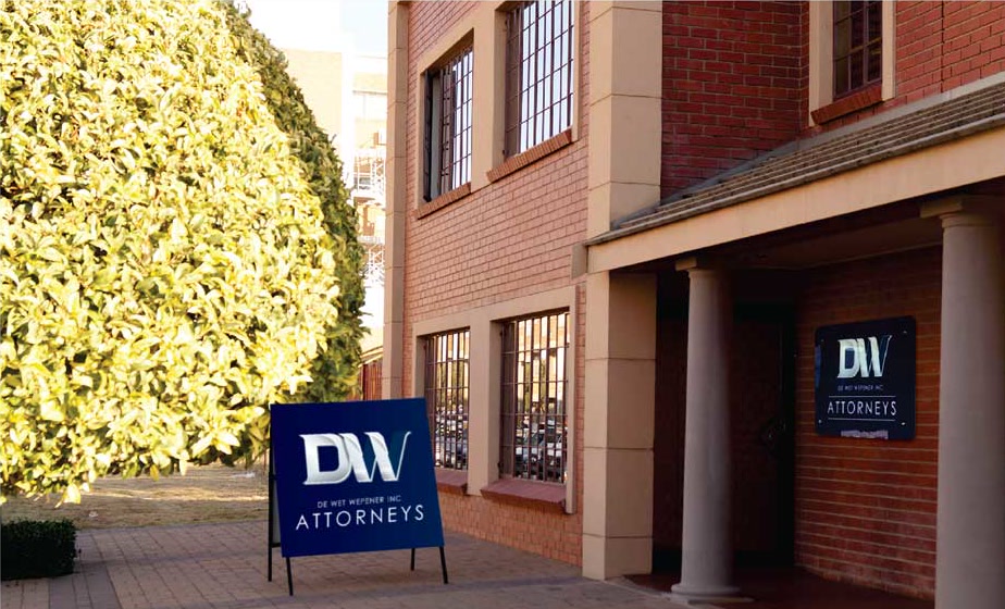 The entrance to the Welkom office, with a DW Attorneys signboard on the paving
                    and a nameplate beside the door.